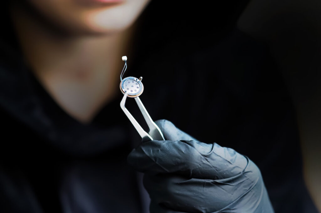 Small microphone of the overhearing device, spy holding a microphone with tweezers, black gloves. Micro listening device
